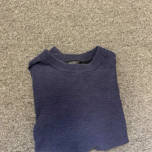 Mörkblå stickad tröja Selected Homme - En stilren mörkblå stickad tröja från Selected Homme. Tröjan har rund halsringning, långa ärmar och ribbade muddar vid ärmslut och nederkant. Perfekt för lager-på-lager och enkel att matcha med jeans 