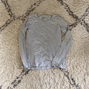 Grå basic långärmad tröja H&M - En enkel och stilren grå långärmad tröja från H&M Basic. Tröjan har rund halsringning och är tillverkad i mjuk bomull, perfekt för lager-på-lager eller som den är. Passar dig som gillar en clean och avslappnad look.