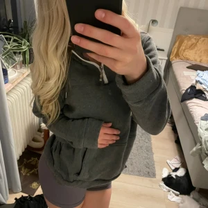 Mörkgrå hoodie med half zip och huva - Mysig mörkgrå hoodie med huva och vit half zip-dragkedja framtill. Tröjan har långa ärmar och huva. 
