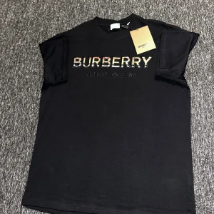 Svart Burberry t-shirt med logga - Svart t-shirt från Burberry i bomull med klassisk rund hals och korta ärmar. Stor Burberry-logga framtill med rutiga detaljer i bokstäverna. Snygg och enkel design som lyfter din outfit med exklusiv känsla.
