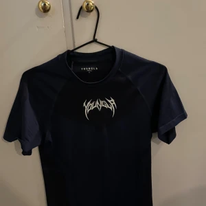 Mörkblå compression t-shirt från YoungLA - Snygg mörkblå compression t-shirt från YoungLA med coolt vitt tryck på bröstet. Modellen är tight och har korta ärmar, perfekt för gymmet eller streetwear. Materialet är lätt och andas, vilket gör den grym för träning. Storlek M men sitter lika bra för S beroende för preferens. Endast testat, original packetering medföljer!