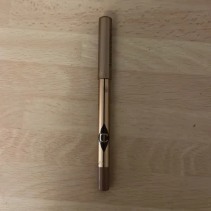 Charlotte Tilbury läppenna Iconic Nude - Läppenna från Charlotte Tilbury i färgen Iconic Nude. Pennan har en snygg beige-brun nyans och kommer i en lyxig guldig hylsa med brunt lock. Perfekt för att definiera och forma läpparna med en naturlig look. Vässad några gånger men fortfarande mycket kvar. 