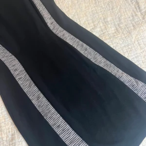 Svart ärmlös klänning från Divided - Svart ärmlös kortklänning från Divided med två grå, randiga paneler längs sidorna som ger en smickrande look. Tight passform och rund halsringning!