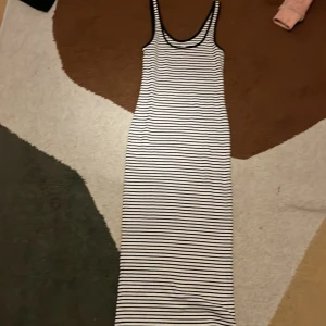 Randig långklänning i ribbad bomull - Säljer en snygg långklänning från Dual i storlek S. Klänningen är vit med svarta horisontella ränder, ribbad struktur och har smala axelband. Den är figurnära och stretchig, perfekt för dig som gillar enkel och stilren design.