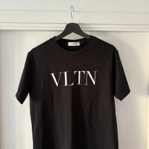 Svart VLTN t-shirt från Valentino - Snygg svart t-shirt från Valentino med stor vit VLTN-logga på bröstet. Klassisk rund hals och korta ärmar. Tillverkad i mjuk bomull, perfekt för en clean och stilren look. Den är liten i storleken så sitter som en M.
