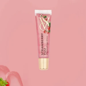 Strawberry Fizz läppglans VS - Glansigt rosa läppglans med jordgubbssmak från Victoria's Secret. Tuben har guldfärgat lock och dekorativa jordgubbar på framsidan. Perfekt för dig som vill ha en söt och fräsch finish på läpparna.
