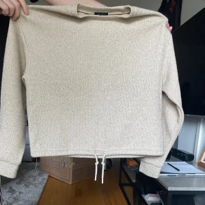 Beige stickad tröja med snörning - Beige stickad tröja från New-Yorker med lång ärm och snörning nertill. Tröjan har en rak passform och är perfekt för lager-på-lager. Mjuk och skön känsla, enkel att matcha med jeans eller kjol. Finns också byxor som tillhör, kan säljas tillsammans eller separat.