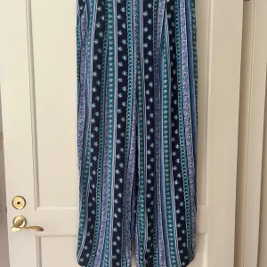Randiga vida retro byxor från Lindex strl 42/44 - Snygga retro vida byxor från Lindex med randigt och blommigt mönster. Byxorna har resår i midjan och har fickor samt är tillverkade i 100% viskos. Storlek 42/44.