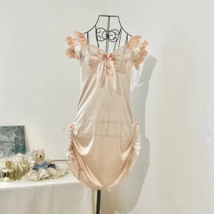 Romantisk ljusorange kortklänning med spets - Supersöt ljusrosa kortklänning med volangärmar, spetsdetaljer och rosett framtill. Klänningen har volangdetaljer på sidorna med små rosetter och vackra spetskanter. (De är dock inte justerbara). Passar storlek 34-36. Dockan har storlek 34.