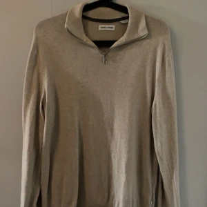 Jack&jones Halvzip  - Beige stickad tröja från Jack & Jones med halv dragkedja i halsen. Tröjan har lång ärm och en klassisk, stilren look som passar perfekt till jeans eller chinos. Mjuk och skön kvalitet, perfekt för lager-på-lager under hösten och vintern.