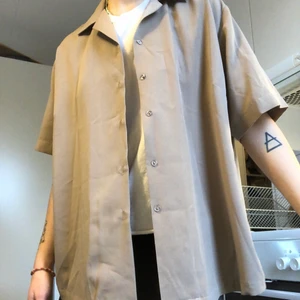 Skjorta  - Tunn beige kortärmad skjorta i glansigt tyg! Längre modell. Lite frakt tillkommer😇 Oklar storlek. Skulle gissa på M.