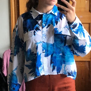 Mönstrad skjorta/blus - Vit skjorta/blus med blått månster. Bred och kort modell. Köpt second hand, i fint skick. Frakt tillkommer.