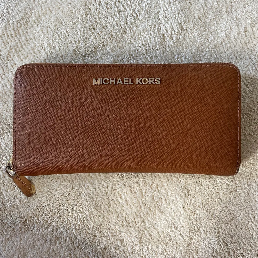 Brun plånbok från Michael Kors med fuldfärgad dragkedja. Fint skick, endast lite sliten i guldfärgen. . Accessoarer.