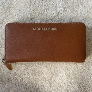 Brun plånbok från Michael Kors med fuldfärgad dragkedja. Fint skick, endast lite sliten i guldfärgen. 