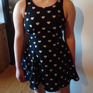 Utsväng sommarklänning med vita hjärtan - Jag säljer min jättefina utsvängda sommarklänning, då den har blivit för liten för mig. Passformen är åtsittande vid överkroppen men svänger ut nedanför midjan. Dragkedja bak, passar storlekarna XS - S. Strykfri, perfekt att bara slänga ner i resväskan.