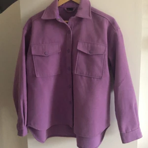 Gina Tricot Tyg jacka strl S - Jag är 160cm och jackan går ner över rumpan, i framsidan går den till höfterna ungefär. Köpt 2021 från Gina Tricot och använd från Augusti-Oktober. Den har Inge defekter alls. En pastell lila färg. Köparen står för frakt. Slutsåld i hemsidan. Köpt på rea och den kostade då ca 150kr. Säljer för att jag inte är förtjust i färgen lika mycket längre.