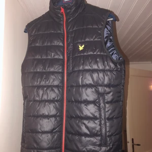 lyle & scott väst - Svart/röd L&S väst, storlek medium. Västen är som ny och skadefri. Säljs då jag har skaffat nya kläder. Nypriset var över 1500 förra hösten ungefär