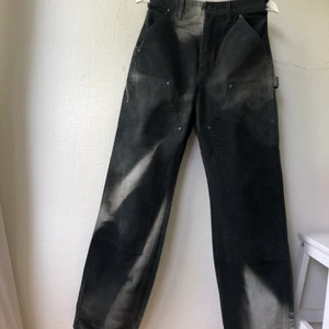 Carhartt byxor 29x34 - Klassiska svarta Carhartt jeans i snickar/arbetar/skate-stil, med flera funktionella fickor och old-school lädermärket på fickan. Färgen har blivit solblekt på flera ställen, ser nästan ut som tie-dye, vilket gör dem väldigt unika!   Storlek enligt lappen är 29x34 men skulle säga att verkliga storleken är något mindre. Passar mig baggy som brukar ha 27-28 i jeans annars.