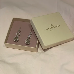 Lily and rose örhängen - Örhängen från Lily and rose, använda endast en gång på balen. Nypris är 1000 kr. Nyskick! De är silvriga med stenar utan färg, passar till allt. Modellen på örhängena heter Amy och färgen är crystal.
