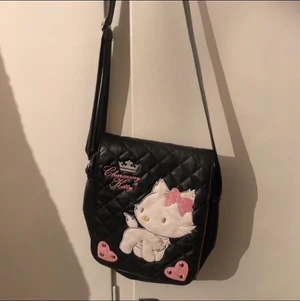 Axelremsväska  - Cool svart axelremsväska, med hellokitty liknande motiv på. Ganska bra skick.