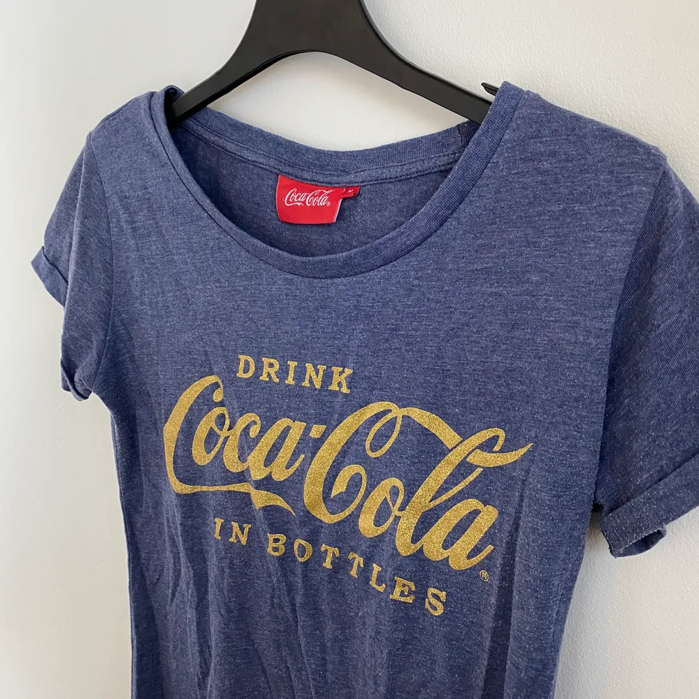 Blå, spräcklig T-shirt med Coca Cola logga på. . T-shirts.