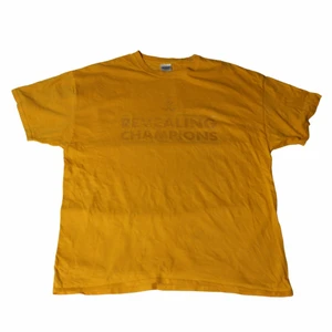 Revealing Champions - Vintage T-shirt - En riktigt Nice gul/orange tröja med ett ganska lågmäld tryck som knappt syns men ändå ger en snygg touch på det hela. Är en segertröja från ett collegelag i USA. Den är thriftad i New York på en thriftstore vi glömt namnet på.