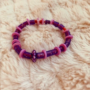 Armband  - Färgerna är lila och rosa det är glittrig pärlor och mitten pärlan är som en lila silvrig diamant 