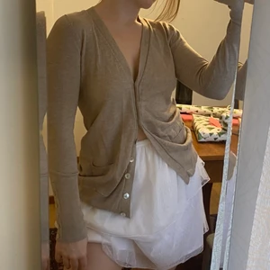 Beige kofta - Mjuk beige kofta med knappar fram och på ärmarna. Den går över höften och är ganska lång i ärmarna. Strl S-M