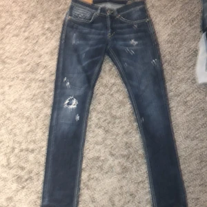 Dondup Jeans Storlek 30 - Mörkblåa Dondup jeans med slitningar - Storlek 30 / Modell: George - Skick: 9/10 Har haft paret i ungefär ett halvår och byxorna har inga slitningar eller hål förutom de som kom - Passfom: Skinny fit - Säljer pågrund av att de inte passar längre - OBS: Jeansen är lite mörkare i verkligen än på bild - Originalpris: ca 2500kr