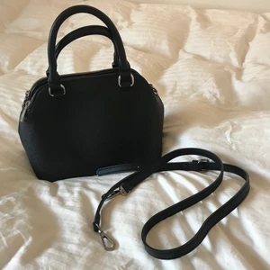 Svart väska - Säljer denna svarta väskan från Zalando. Den är i jättefint skick och använd ett fåtal gånger. Cirka 30cm lång, 20cm hög och 15cm bred så den rymmer mycket. Den har tre olika fack, två med dragkedja och ett med knapp. Axelband tillkommer. 