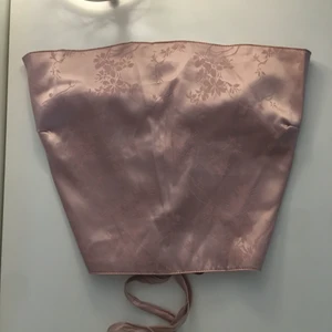 Topp  - Jättesöt ljusrosa (lite åt det lilla hållet) topp i satin material med blommigt mönster. Aldrig använd, går att skjutsera som önskas med banden i ryggen. Storlek M. 