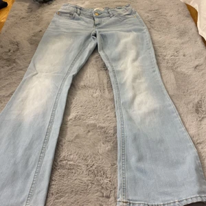Utsvängda jeans från Lindex - Ljusblåa, utsvängda jeans med guld detaljer. Stl 152/11-12år