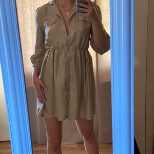 Vila klänning - Skjortklänning. Resår i midjan. Silkeslikt material. Knappar på hela framsidan så du kan justera hur öppen eller stängd den ska vara. Jag på bilden är 168 cm lång.