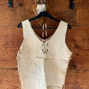 Linne / Topp i mjukt skinn. Ny / Oanvänd. - Ljus beige Linne / Topp med ’råa’ kanter i skinn. Storleken går att ändra något beroende på hur man vill att Linnet / Toppen skall bäras. Mått: ärmhåla till ärmhåla 2x43 cm, ärmhåla till nederkant ~ 33 cm. Uppskattad storlek: ~ 36/38. Ny/Oanvänd. Fraktkostnad: 66kr. Äkta skinn.