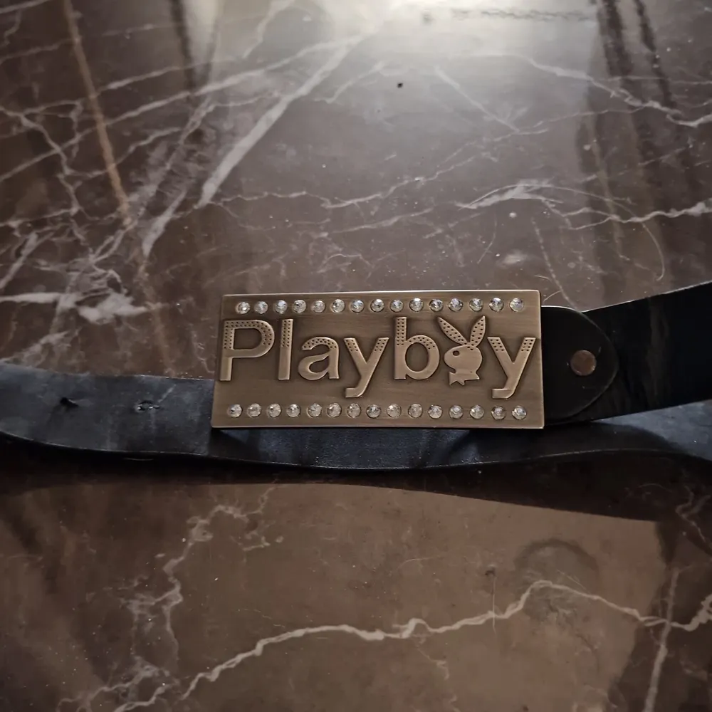 Ett svart skärp med playboy märket. 97 cm långt skärp, 3.7 cm brett. Playboyloggan är 11 cm lång och 4.8 cm bred.. Accessoarer.