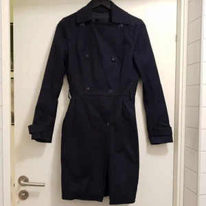 Mörkblå trenchcoat dam - Knälång mörkblå Trenchcoat för dam i storlek 34 från InWear i fint skick. Modellen smalar av i midjan och går sedan ut lite. Knapparna är svarta med ankarmotiv. Tillhörande midjeband skickas med. Sparsamt använd. 