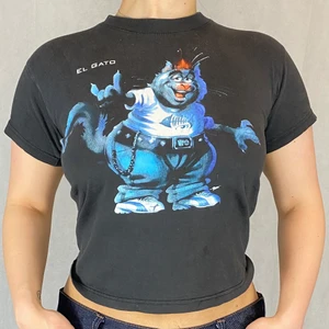 Baby Tee  - El Gato baby tee i okej skick! Barnatorlek 130-140. Modellen använder vanligtvis storlek S/M och är 169cm långt. Från No Problem Sportswear. 100% bomull. Mått:  Axeln till axeln 40cm, ärmlängd 13cm, bystbredd 43cm, armhåla till armhåla 45cm och längd 50cm. FRI FRAKT 