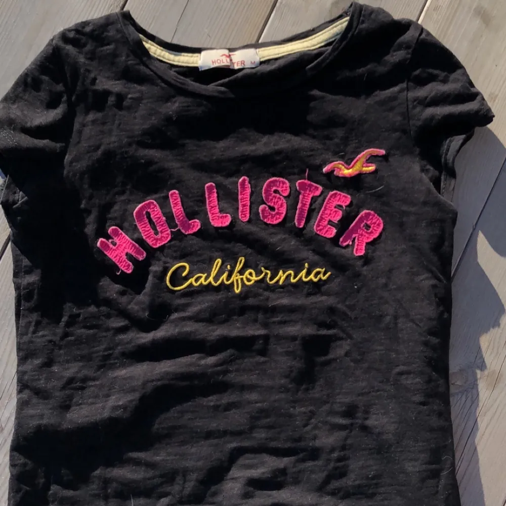 En svart rätt tajt t-shirt från Hollister. Rosa märke på bröstkorgen. Väl använd men i fint skick.. T-shirts.