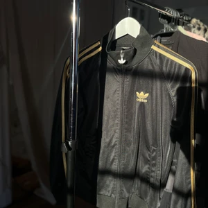 Adidas zip-up hoodie - Svart/guldig tröja från adidas, haft denna väldigt länge så den är väl använd men inget trasigt eller liknande. ☺️ Köparen står för eventuell frakt!✌🏼 