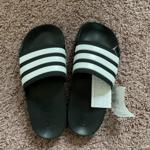 Adidas tofflor  - Heeeelt oanvända Adidas tofflor🖤🖤 köpte i fel storlek o lämnade aldrig tillbaka, därför helt oanvända med prislappen kvar🖤🖤 BUDA MED MINST 10kr
