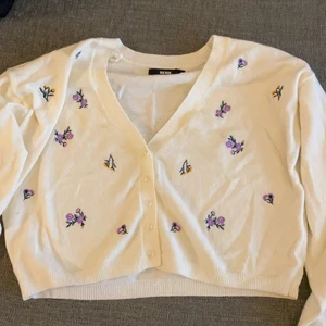 Cardigan med detaljer  - En vit cardigan med lila och gula blom detaljer. Jätte mysig i mjukt ”stickat” material, från bikbok. Den är använd 1 gång och köpt för inte så länge sedan.✨ köpare står för frakt kommentera eller kontakta mig för intresse✨