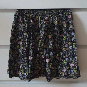 Blommig kjol  - En svart kjol med färgglada blommor. Kjolen kommer från monki. Frakten ingår alltid I priset :) 