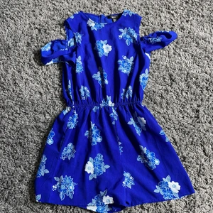 Blå jumpsuit - En blå jumpsuit med några blommor på, dragkedja på baksidan. Använd max 2 gånger och är i fint skick. Priset kan diskuteras vid snabb affär, och om fler bilder önskas så kan det fixas.:)