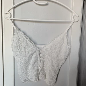 Spetslinne - Vitt Spetslinne med pärlor som knappar. Man öppnar/stänger alltså toppen genom pärlknapprna. Nämn ett pris som känns rimligt för dig vid intresse! Meddela mig för fler bilder eller frågor!