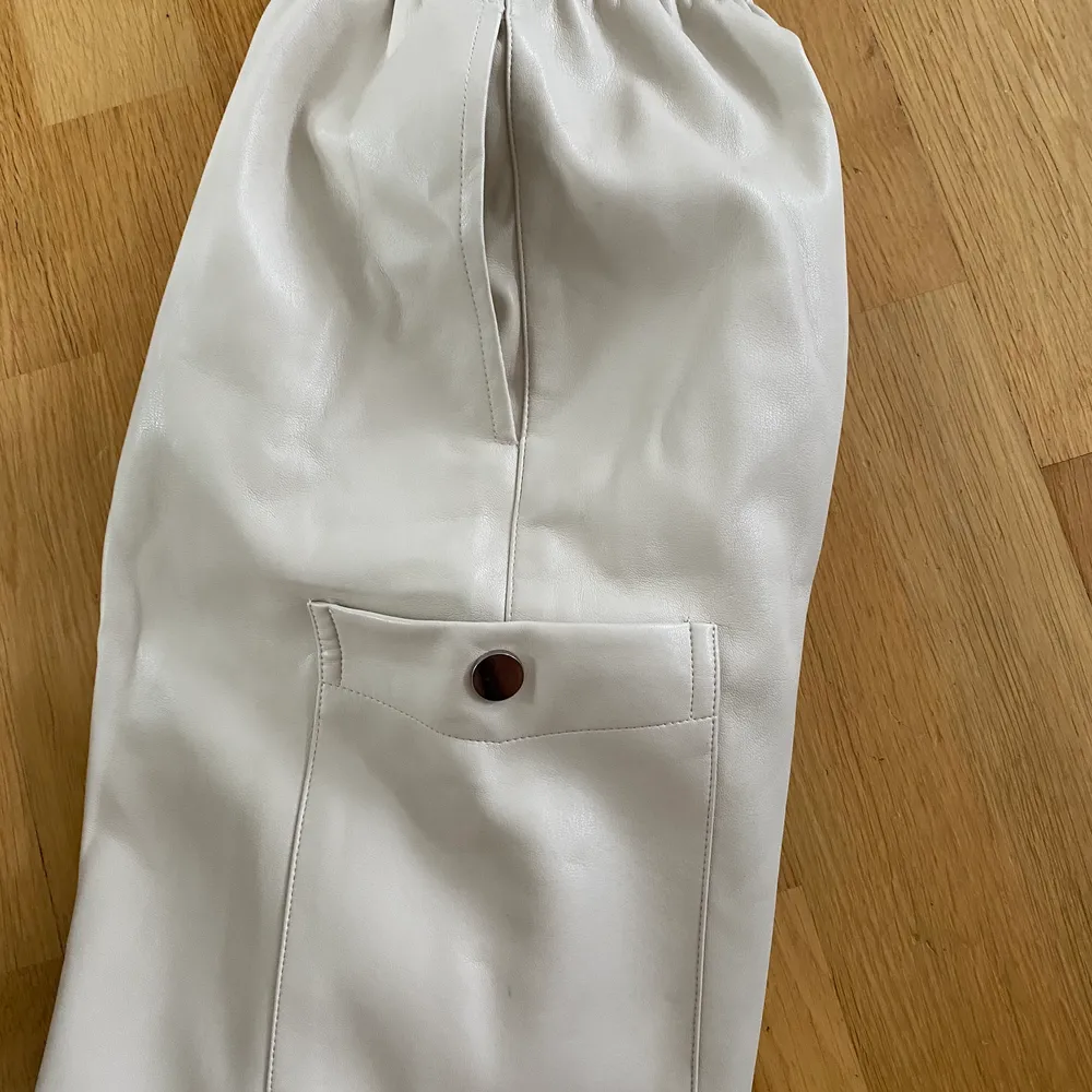 Ett par beiga byxor i läderimitation, som är lite lösare i modellen. De har två fickor på vardera sida och även en knapp längst ned på båda sidorna. Har använts en gång och är från Zara.. Jeans & Byxor.