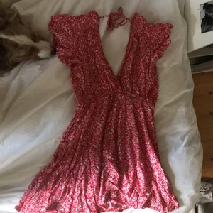Helt ny röd blommig klänning från shein - Helt ny oanvänd röd blommig klänning från shein i storlek S. Väldigt unik klänning med djup vringning i ryggen och med ett band att knyta rosett i nacken. Den visar inte för mycket där fram då den korsas. Superskönt och somrig klänning 💕
