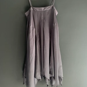 Glättad klänning - Söt klänning i kortare utsvängd modell med en asymmetrisk kant och spaghettiband. Klänningen är grå och har en glättad yta. Väldigt fint skick. Storlek S. Köpare står för frakt