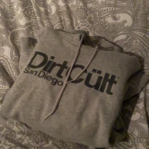 Grå Dirtcult hoodie  - Grå dirtcult hoodie i bra skick. Använd hyfsat mycket men enda negativa är ett litet hål på vänster axel (se bild) Storlek L men väldigt liten i storlek, passar mer M/S. Nypris 699kr men säljer för 150kr. Köparen står för frakt.