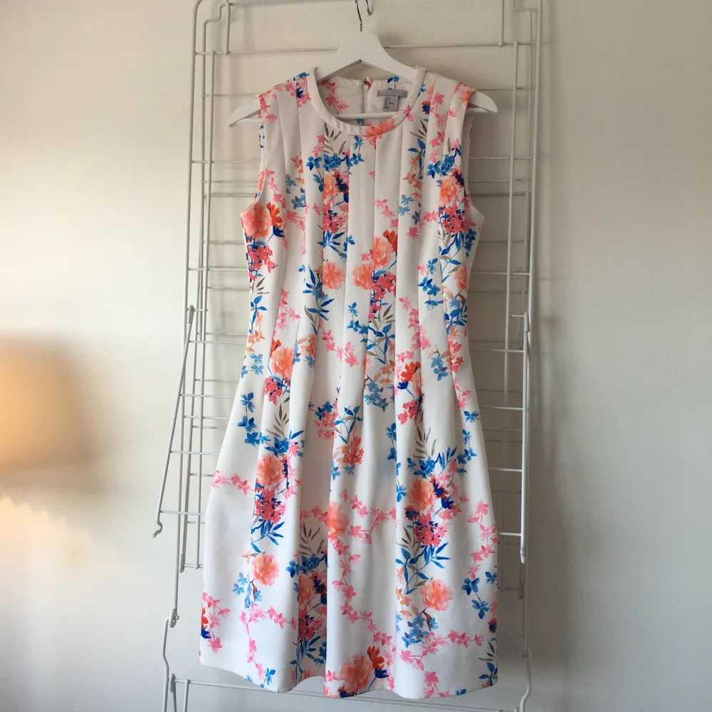 Size 38 dress with length from neck down 88cm. The waist is fitted around ~82cm but should work a few centimetres less as well. Condition is used but is still good quality! The dress has a little stretch in it and is white with Pink, Orange and Blue flowers. The back has a hidden zipper which goes down the back. . Klänningar.