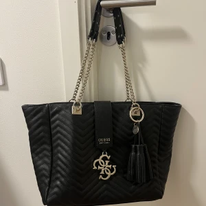 Guess Handväska - Jättefin stor handväska från Guess med mycket guld detaljer! Supermycket fack inuti så finns gott om förvaring. Perfekta Handväskan.